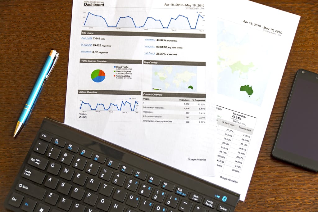 Flatlay of a business analytics report, keyboard, pen, and smartphone on a wooden desk.